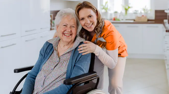 Nurse standing next to an elderly lady who is in a wheelchair.