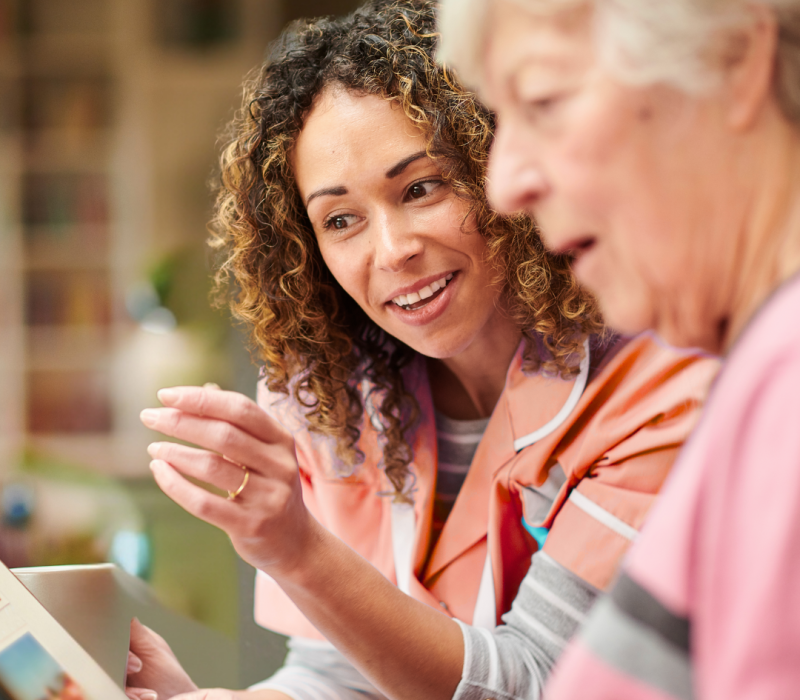 A woman with curly hair showing an elderly lady how to use the new client management software in a home